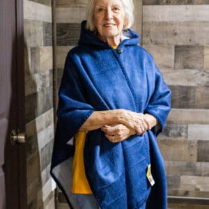 A woman in blue and yellow poncho standing next to wall.