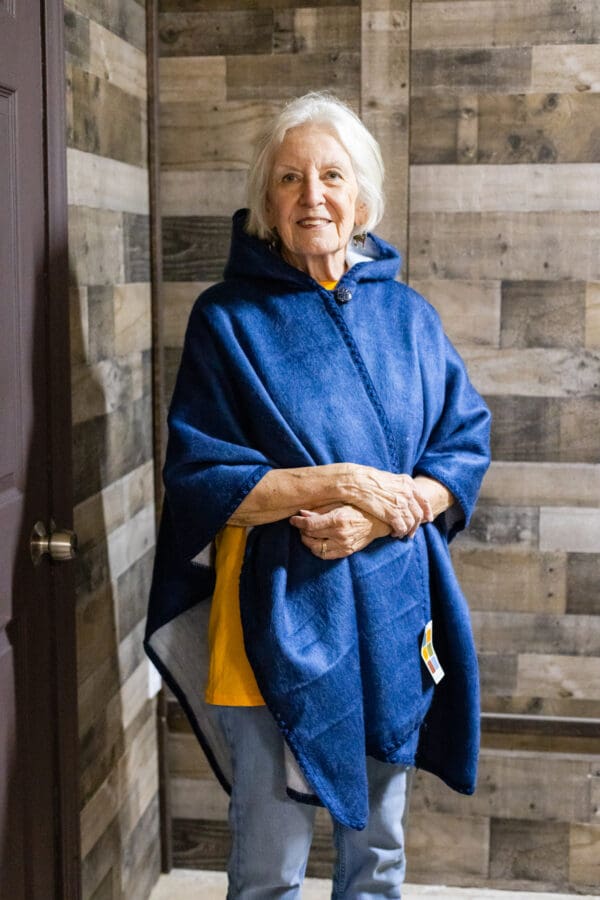 A woman in blue and yellow poncho standing next to wall.