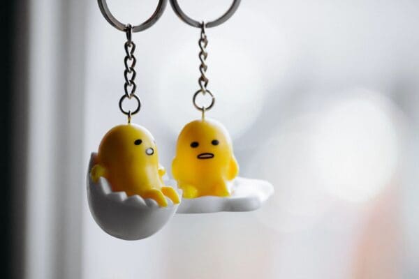 Two keychains with a yellow chick and an egg.